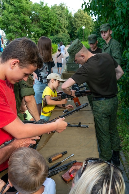 Grodno Wit-Rusland 10 juli 2022 Een kind met een Kalashnikov-aanvalsgeweer in zijn handen op een vuurwapententoonstelling Een menigte mensen onderzoekt vuurwapens, pistolen, machinegeweren, mijnen en munitie