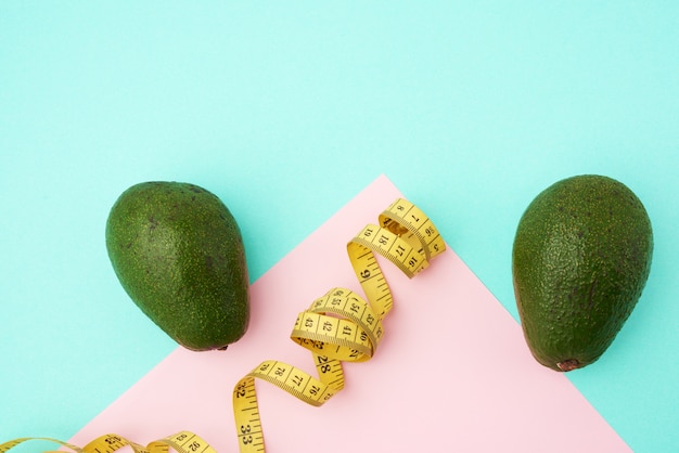 Groen avocadofruit en een gedraaide gele meetlint op een groenroze