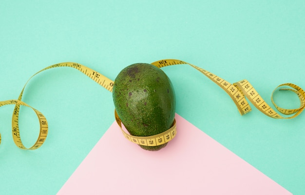 Groen avocadofruit en een gedraaide metende gele band op een groen roze achtergrond