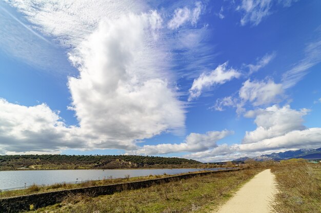 Groen berglandschap met blauw meer, onverharde weg en grote wolken aan de hemel, lentesfeer. guadalix madrid. europa.