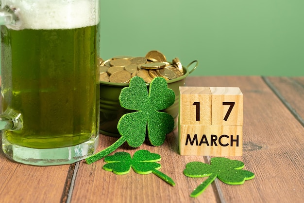 Groen bier naast een pot met munten en verschillende klavers op tafel en de datum van St. Patrick's