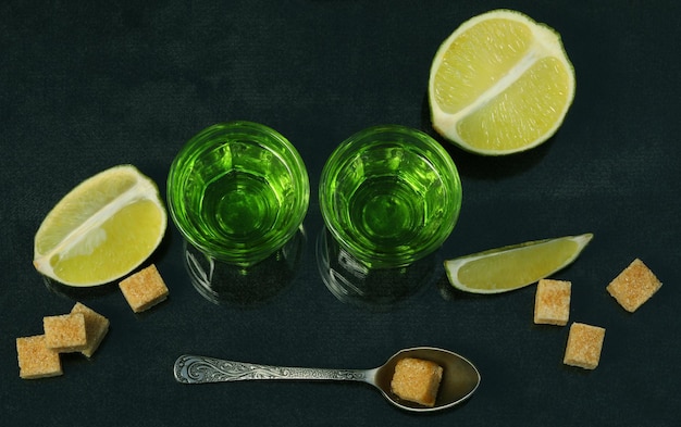 groene absintdrank op de zwarte achtergrond met suiker en limoen