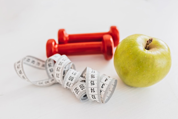 Groene appel, centimeter en rode halters. Gezondheidszorg, dieet en sportconcept