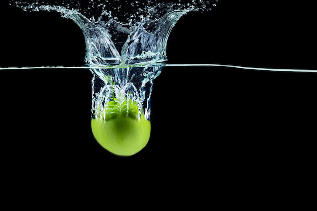 Groene appel die in water met een plons valt tegen donkere achtergrond
