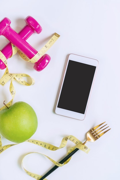 Foto groene appel, halter, meetlint en slimme telefoon op witte tafel. selectie van gezonde voeding en lichaamsbeweging voor een goede gezondheid. biologisch voedsel, dieet, afvallen concept. bovenaanzicht, kopieer ruimte.