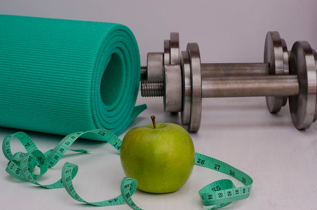 Groene appel met halters, een tapijt en een tape. Vrouwelijke fitness.