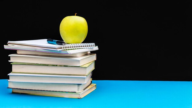 Groene appel op stapel boeken en blocnotes tegen bord Ruimte voor tekst Terug naar schoolconcept