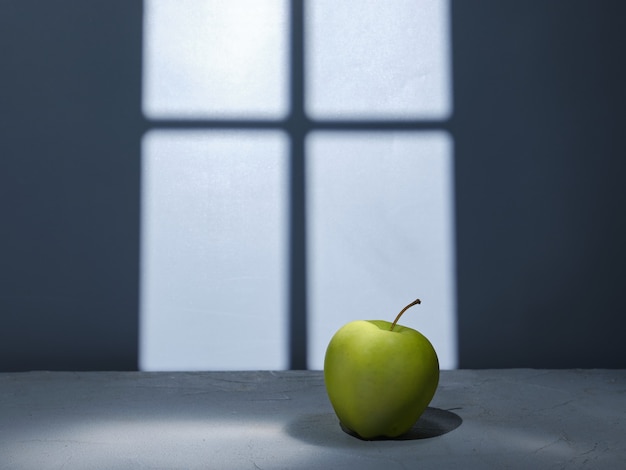 Groene appel op tafel tegen de achtergrond van de muur met licht uit het raam