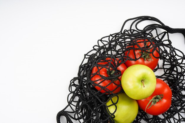 Foto groene appels en rode tomaten in zwarte netto zak op witte achtergrond