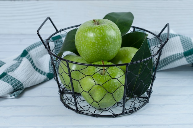 Groene appels met bladeren in de metalen zwarte mand op een witte ondergrond.​