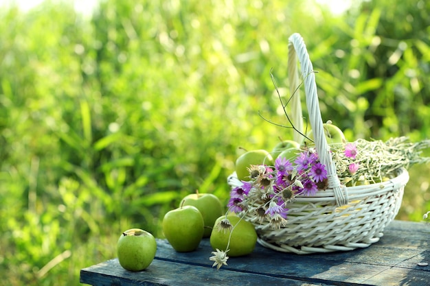 Groene appels met boeket van wilde bloemen op houten tafel buiten