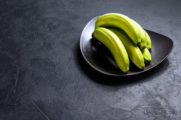 Groene bananen op een plaat. Zwarte achtergrond. Bovenaanzicht. Ruimte voor tekst. Tropisch fruit