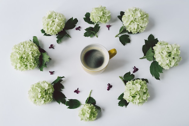 Groene bloemen in de vorm van een cirkel die rond de gele Kop met koffie op witte achtergrond liggen