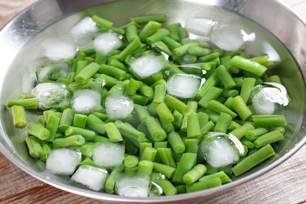 Groene bonen in een vergiet. Gekookte of geblancheerde groenten in ijswater op een houten tafel