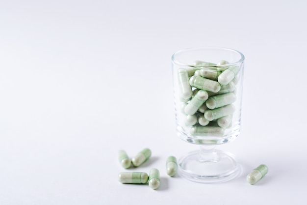 Groene capsule pillen in een cocktailglas op een witte achtergrond