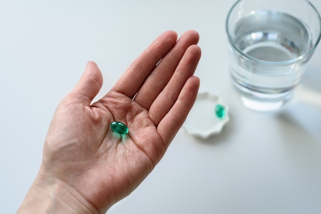Groene capsule, tablet in hand met glas water op witte achtergrond, behandeling, placeboconcept, bovenaanzicht