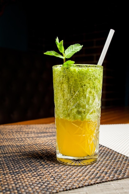 Groene cocktail met vruchtvlees en stro. Groene cocktail met komkommer en peterselie als gezond zomerdrankje op een donkere achtergrond.