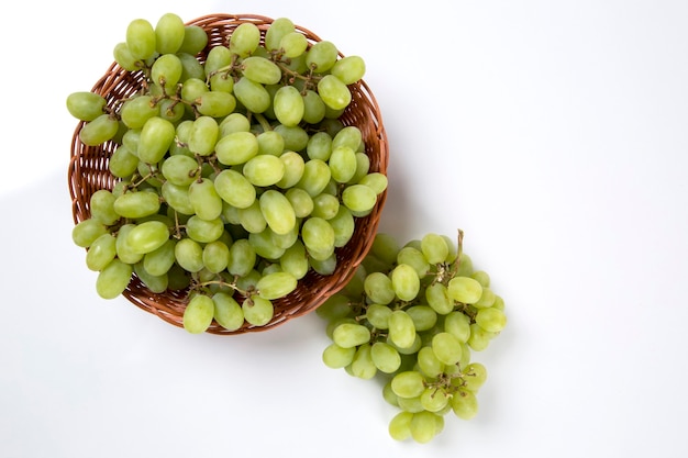 Groene druiven in een mand over een witte ruimte.