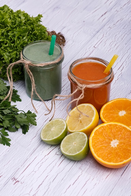 Groene en oranje detox coctails staat op witte tafel met fruit en groenten