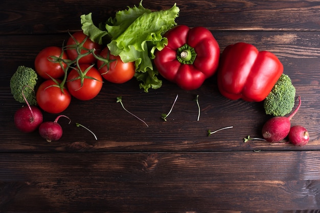 Groene en rode verse groenten, rode paprika, radijs, tomaten, groene salade zijn op een donkere houten tafel, plat leggen.