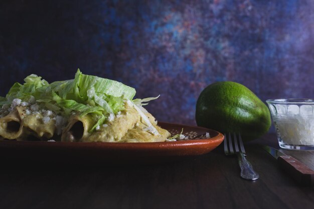 Groene Enchiladas met sla geserveerd in een kleischotel op een houten tafel.