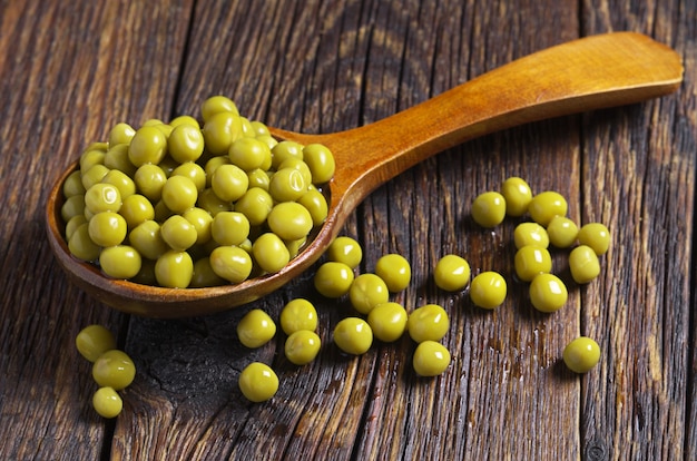 Groene erwten ingeblikt in lepel op oude houten tafel