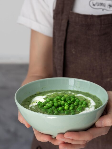 Groene erwtensoep in een kom die door handen wordt vastgehouden