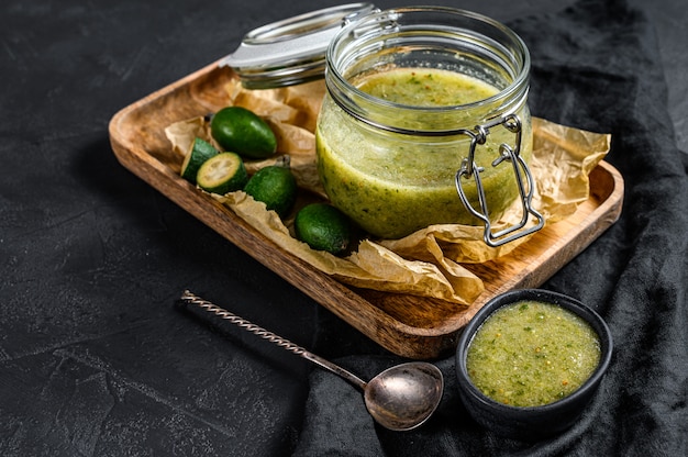 Groene feijoa jam op een houten snijplank in een glazen pot. natuurlijke zelfgemaakte dessert. zwarte achtergrond. bovenaanzicht