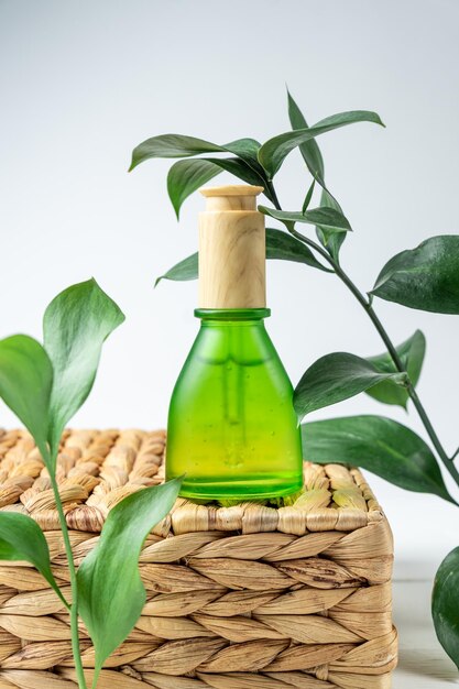 Groene frosted glazen cosmetische fles met een druppelaar op een achtergrond van natuurlijke materialen met tropische bladeren. Natuurlijk cosmeticaconcept, natuurlijke etherische olie en huidverzorgingsproducten.