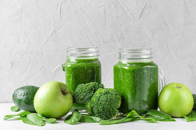 Groene gezonde detox smoothie met verse groenten en fruit in potten op witte muur. Gezond detoxontbijtconcept. detailopname