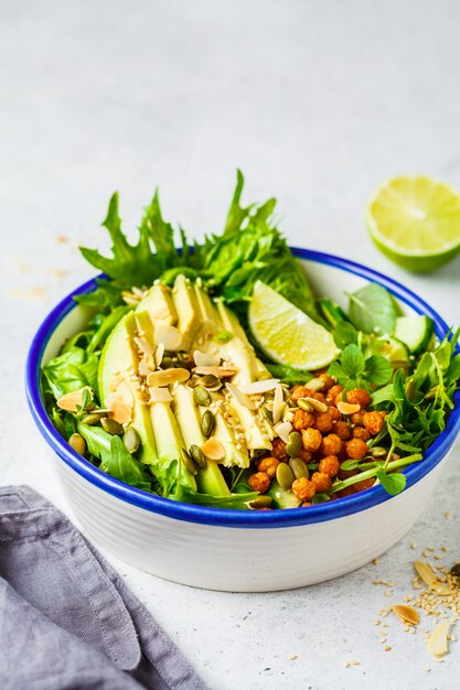 Groene gezonde salade met avocado, gebakken kikkererwten en zaden in witte kom.