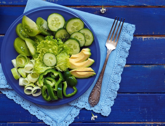 Groene groenten en fruit - sla, komkommer, prei, avocado, appel en groene paprika op blauwe houten ondergrond