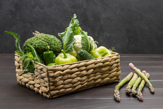 Groene groenten in rotanmand. Asperges op tafel. Houten achtergrond. Ruimte kopiëren