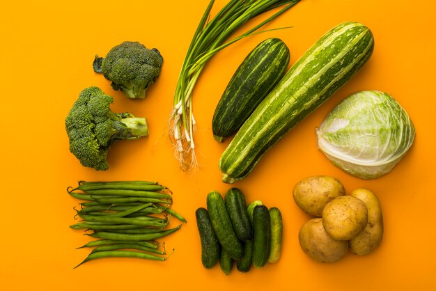 Groene groenten op gele achtergrond kleurrijk concept, bovenaanzicht, aardappelen, broccoli, komkommer, ui, kool, courgette, bonen