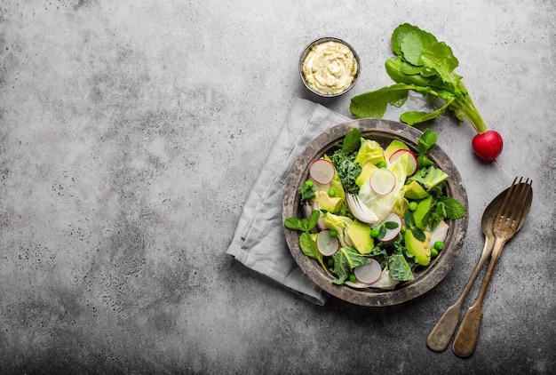 Groene groentensalade met avocado, boerenkool, kiemkruiden in rustieke kom geserveerd met saus, grijze betonnen ondergrond, close-up, bovenaanzicht. gezond schoon eten, dieet/detox concept met ruimte voor tekst