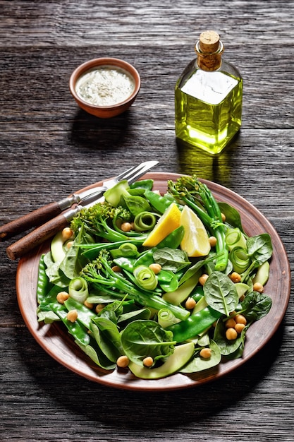 Groene groentesalade van gebakken tenderstem broccoli peultjes avocado komkommer kikkererwten baby spinazie met olijfolie dressing geserveerd op een bruine kleiplaat op een donkere tafel close-up bovenaanzicht