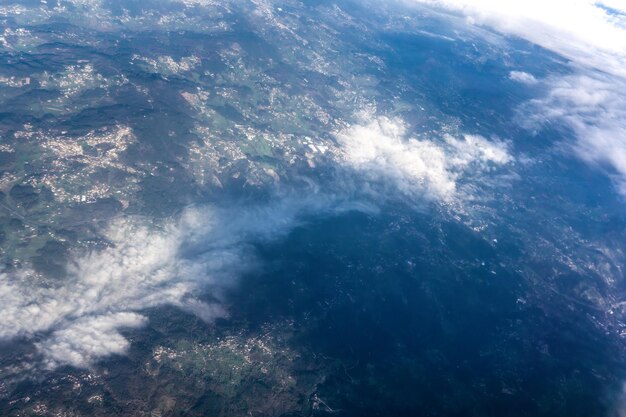 Groene heuvels met een verstrooiing van witte huizen in de mist bedekt met wolken Uitzicht vanuit het vliegtuig raam