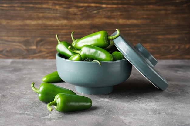 Groene jalapeno pepers in een keramische kom op een grijs-houten achtergrond.