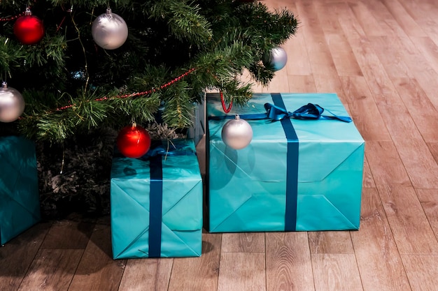 Groene kerstboom met versieringen en cadeautjes eronder in loft interieur. Grote blauwe dozen in een cadeauverpakking met een lint. echte natuurlijke spar.