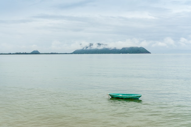 Groene kleine fishng boot geparkeerd aan de kust van Prachuap Bay met mist op Khao Ta Mong Lai Forest Park-achtergrond, Thailand