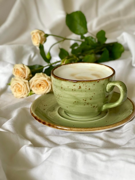 groene kop koffie en rozen op het bed, koffie in de ochtend op het laken, foto van de telefoon