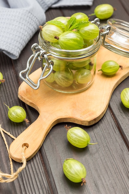 Groene kruisbessen in glazen pot op snijplank. grijze servet en kruisbessen op tafel. donkere houten achtergrond. bovenaanzicht