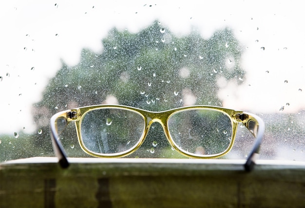 Groene leesbril boven het regenachtige raam