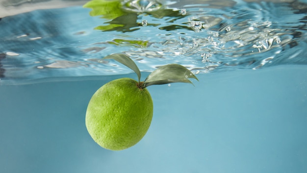 Groene limoen onder water met een spoor van transparante bubbels