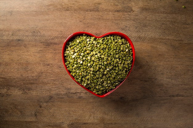 Groene linzen in een hartpot op houten achtergrond. Eetbare rauwe peulvruchten van de peulvruchtenfamilie.