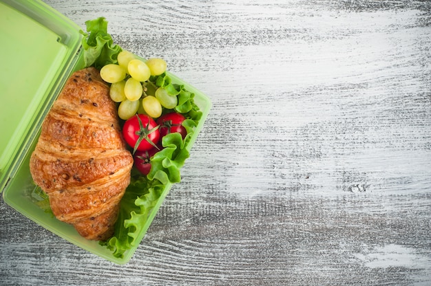 Groene lunchbox met croissant, salade