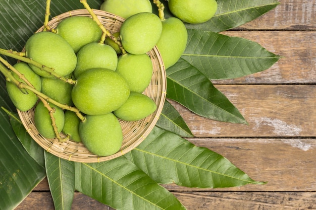 Groene mango's in mand en bladeren op de vrije ruimte van de houten vloer.