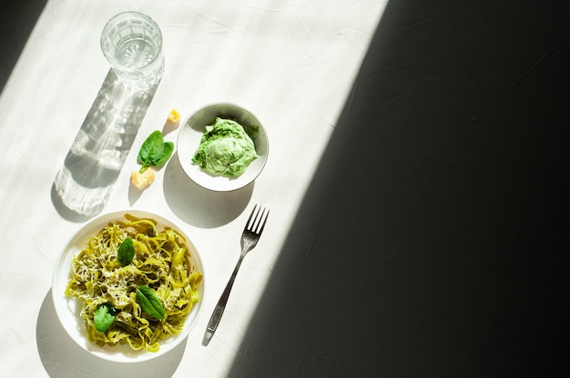 Foto groene noedels met spinazie en parmezaanse kaas in een witte plaat op een witte tafel hard licht en shad...