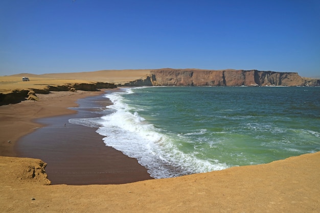 Groene oceaan, rood strand, gele klif en blauwe hemel bij Paracas National Reserve in Ica, Peru