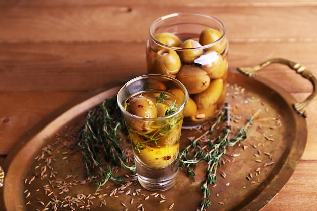 Groene olijven in olie met kruiden en rozemarijn in glazen potten op houten tafel